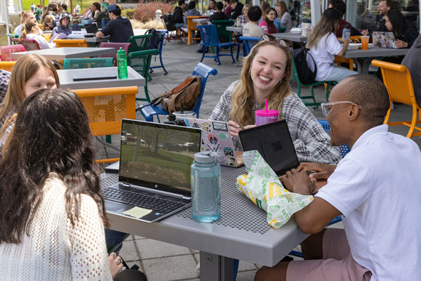 Students sit at a table outside talking and laughing at Binghamton University.