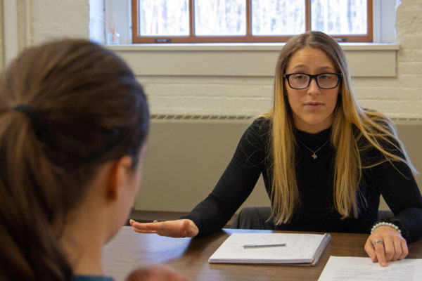Female professional talks to female student at a table.