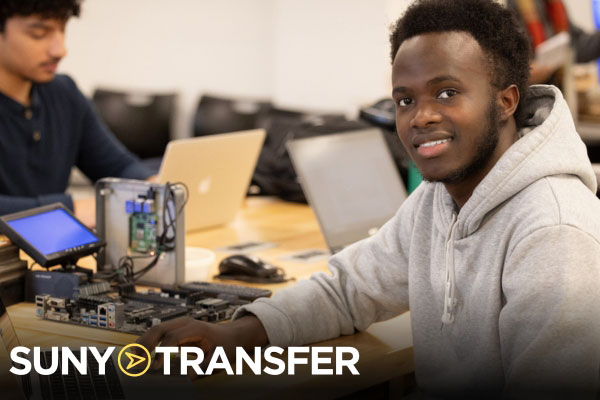 SUNY Transfer wordmark with wale student smiling form his seat at a table in college lecture hall.