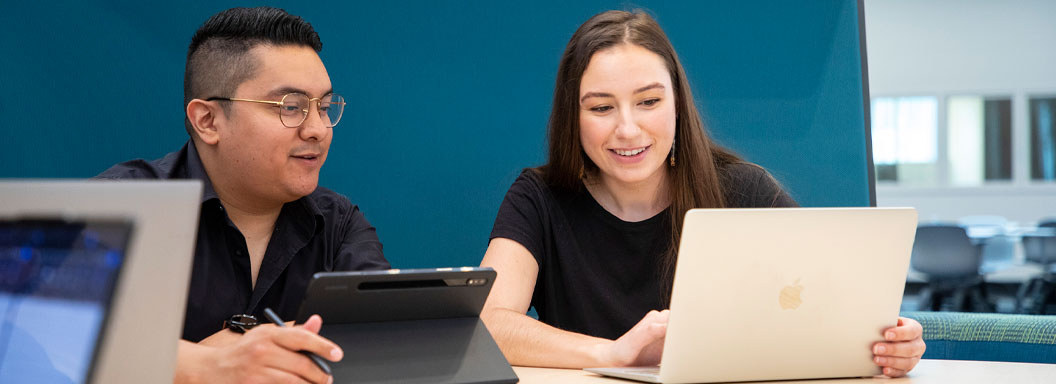 Two students on their laptops study at a table.