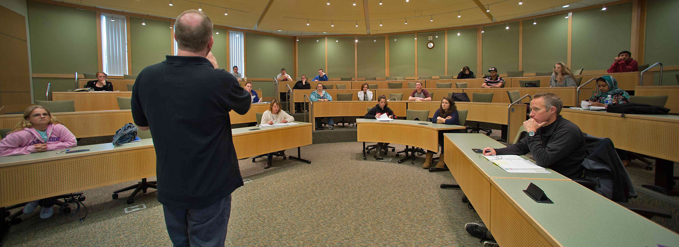 professor stands before class in lecture setting